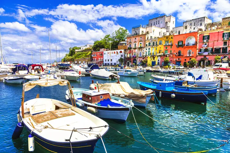 Barche ormeggiate nel porto di Procida con edifici colorati sullo sfondo.